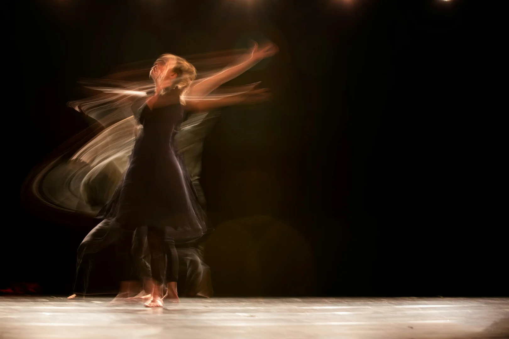 A dancer in a dark, flowing dress caught mid-whirl with streaking trails of light and motion, illustrative of Alice's tumble into Wonderland