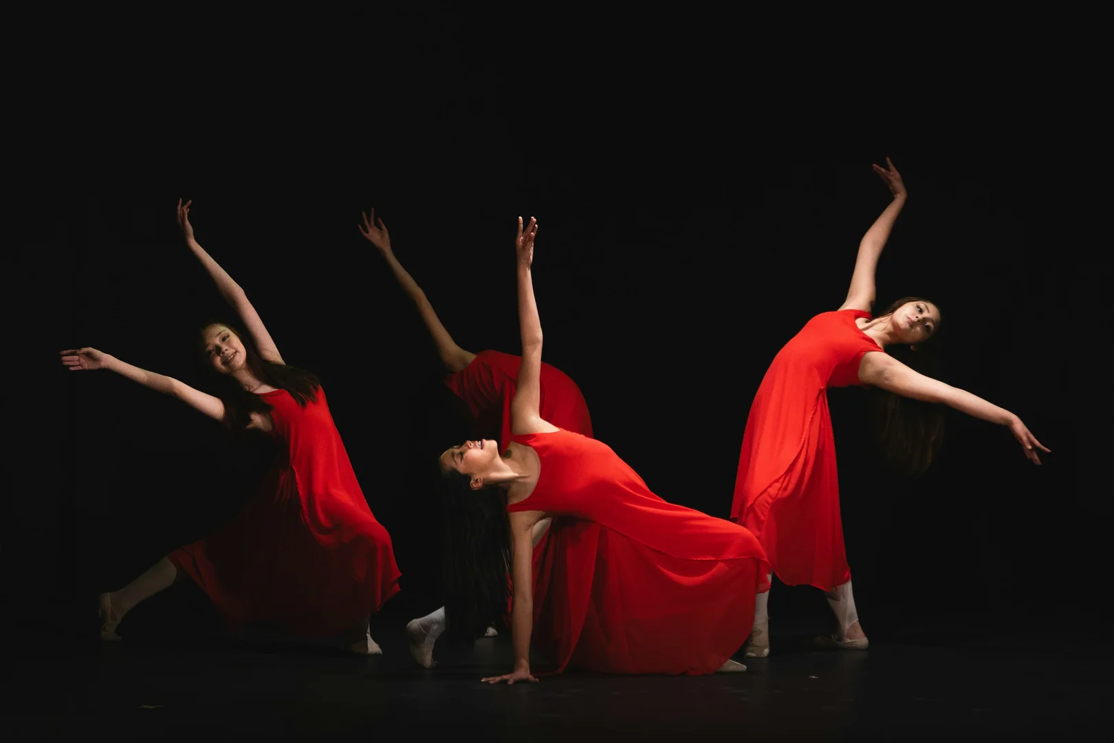 Dancers in flowing red costumes caught in sharp, backlit poses against total darkness, illustrative of Grand Finale's stark imagery of conflict and mortality