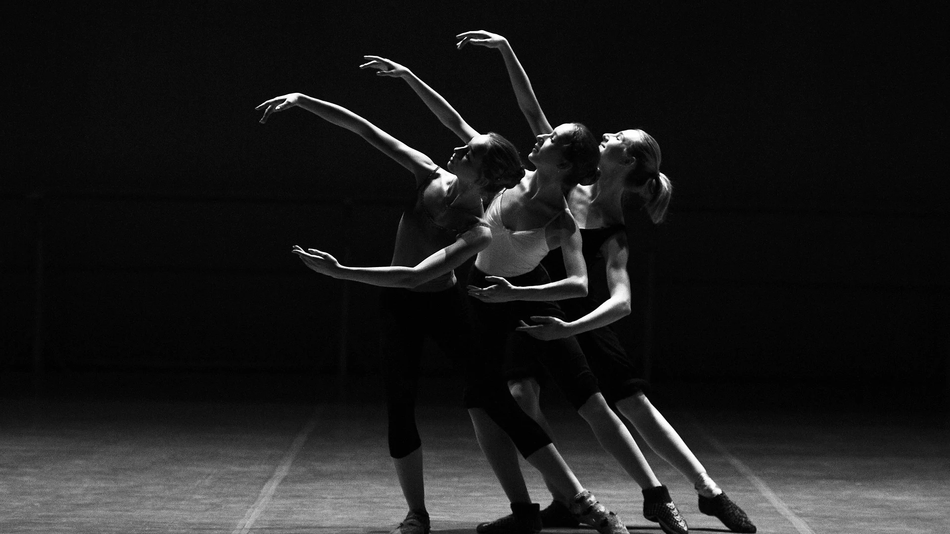 A trio of dancers in dramatic dark lighting, illustrative of Crystal Pite's ensemble-driven physical theatre