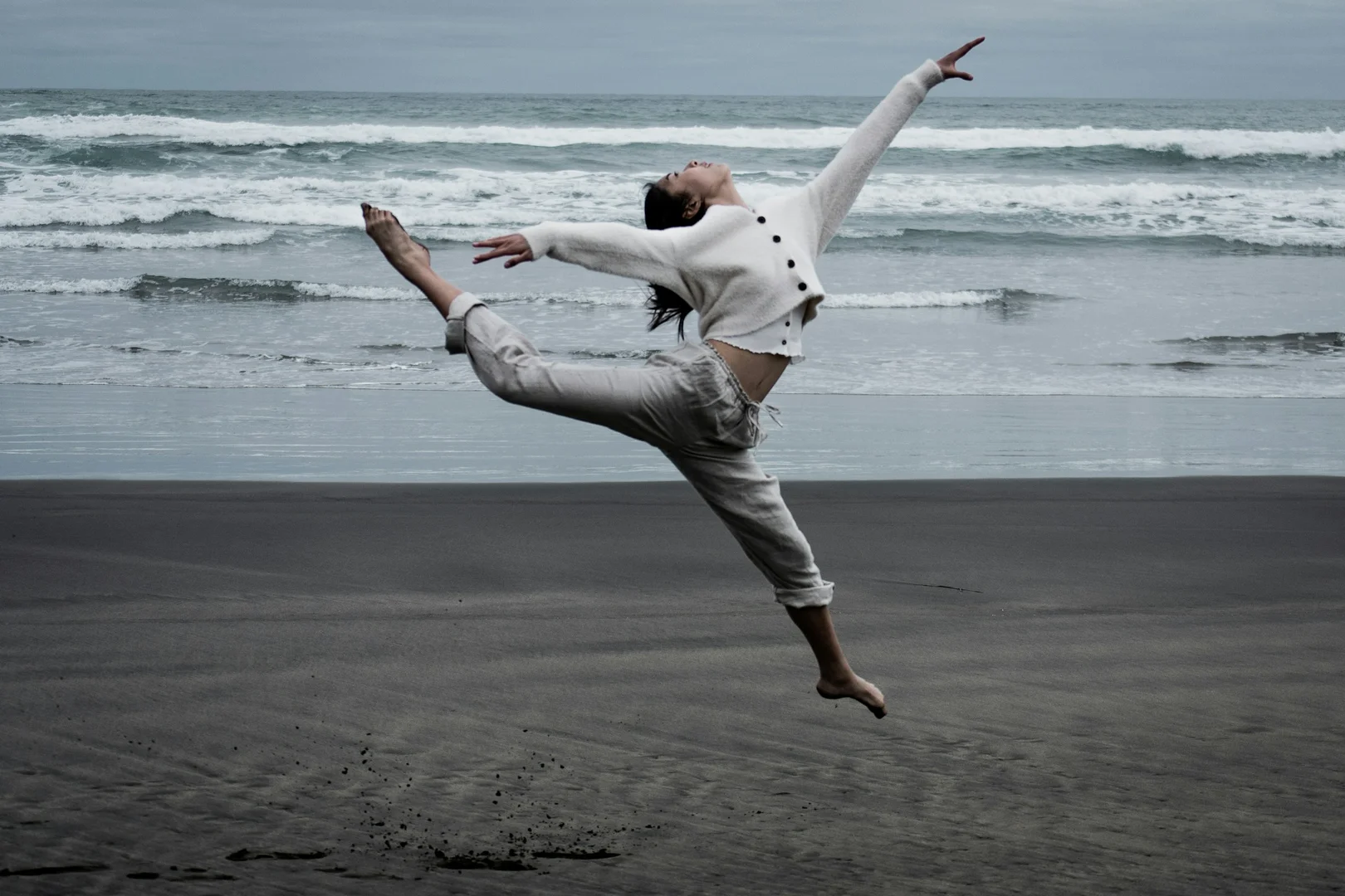 A partnered dancer in an extreme extension on a dark stage, illustrative of Crystal Pite's choreographic style