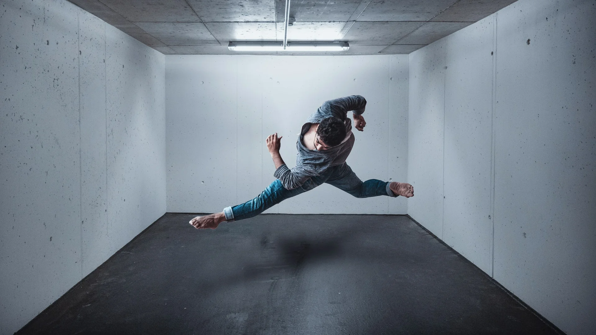 A dancer in a sharp, tucked leap through a concrete corridor, illustrative of William Forsythe's choreographic style